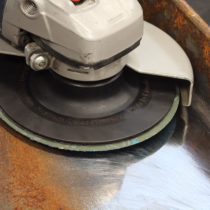 GRFA11580_4 - Alpha Tools Close-up of an angle grinder spinning a grinding wheel against a rusted metal surface.
